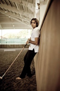 Polo player Ameer Jumabhoy poses barefoot, stangin in the arena holding is mallet.