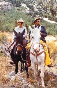 Son Craig London rides a bay horse and Herb London a grey in a mountainside environment.