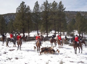 Hunters convene on horseback with their pack of hounds in a snowy, mountain region.