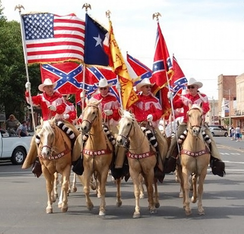 A unit of four Palomino horses parades with brightly colored flags.