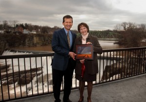 Tom Struzzieri and Susan Colchamiro stand on a fenced patio against the backddrop of a waterfall.