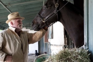 Nick Nolte pets a black horse in a barn.