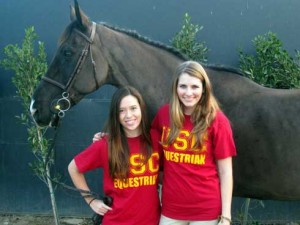 Two girls in red USC t-shirts in front of a bridled but unsaddled horse.