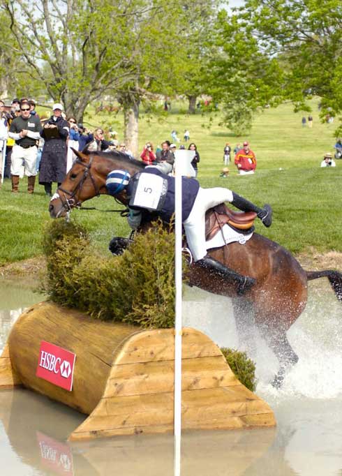 Karen O'Connor clings to her horse's side through the water.