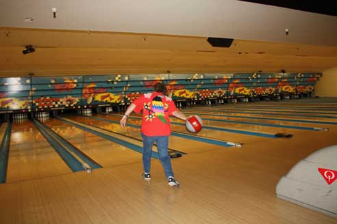 Woman bowling in a red shirt with a parrot on the back.