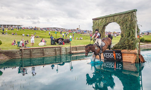 Horse and rider coming through the Keyhole jump, a hole of circular brush jump in water.