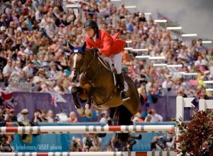 Beezie Madden and her dark chestnut mare, Via Volo, fly over a vertical jump.