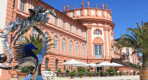 Coral-colored alace at Wiesbaden with Global Champions Tour trophy looming in foreground.