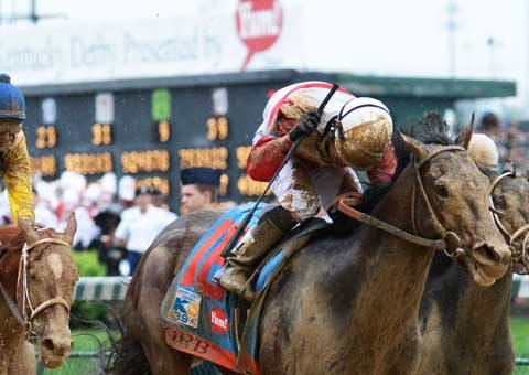 Jockey Joel Rosario raises his crop in victory as a mud-splattered Orb crosses the finish line at the Kentucky Derby.