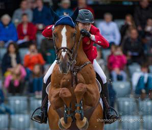 Lucy Davis in her red team USA coat takes a jump on Barron, a chestnut gelding.