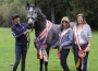 Trainer Susann Regalmuto stands with her champion pupil, the ribbon-strewn gray horse Fuego Amor, and his two owners.