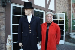 Nadine Tilley, in a bright red jacket, stands beside a manequin of a "groomsman" in a top hat and tails.