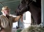 Nick Nolte pets a black horse in a barn.