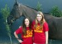 Two girls in red USC t-shirts in front of a bridled but unsaddled horse.