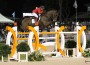 Wearing a red jacket, Meredith Michaels Beerbaum and her bay horse leap a bright yellow and white jump.