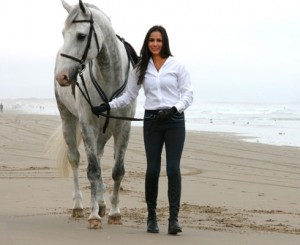 Girl walking a grey horse on beach while wearing black Lo-Ride breeches.