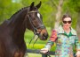 Woman in a brightly-colored coat of geometric pattern leads a bay horse.