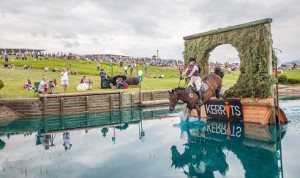 Horse and rider coming through the Keyhole jump, a hole of circular brush jump in water.