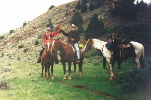 Marc and Royan Herman high-five on horseback in a green pasture.